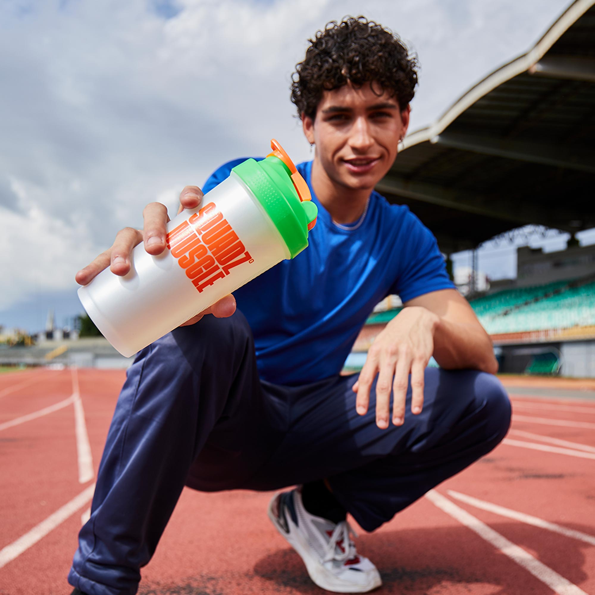 Coqueteleira SQUADZ MUSCLE Branco Pérola com Laranja 600ml — Homem agachado na pista