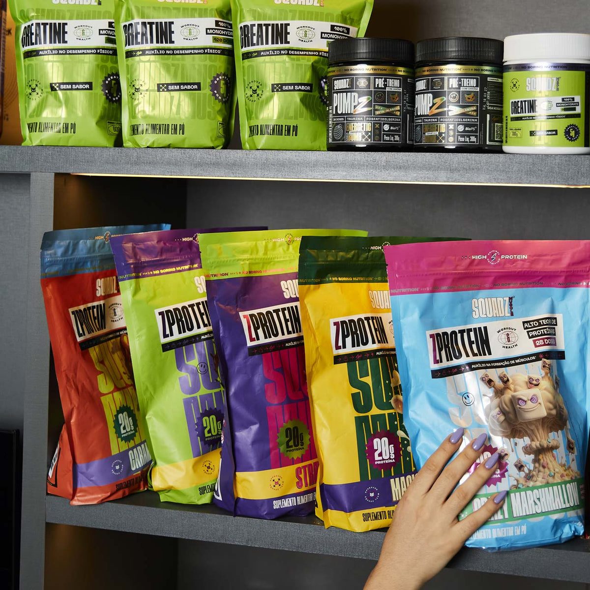Prateleira com a linha completa SQUADZ MUSCLE: potes de Creatine em cima e sacos de ZPROTEIN de vários sabores embaixo