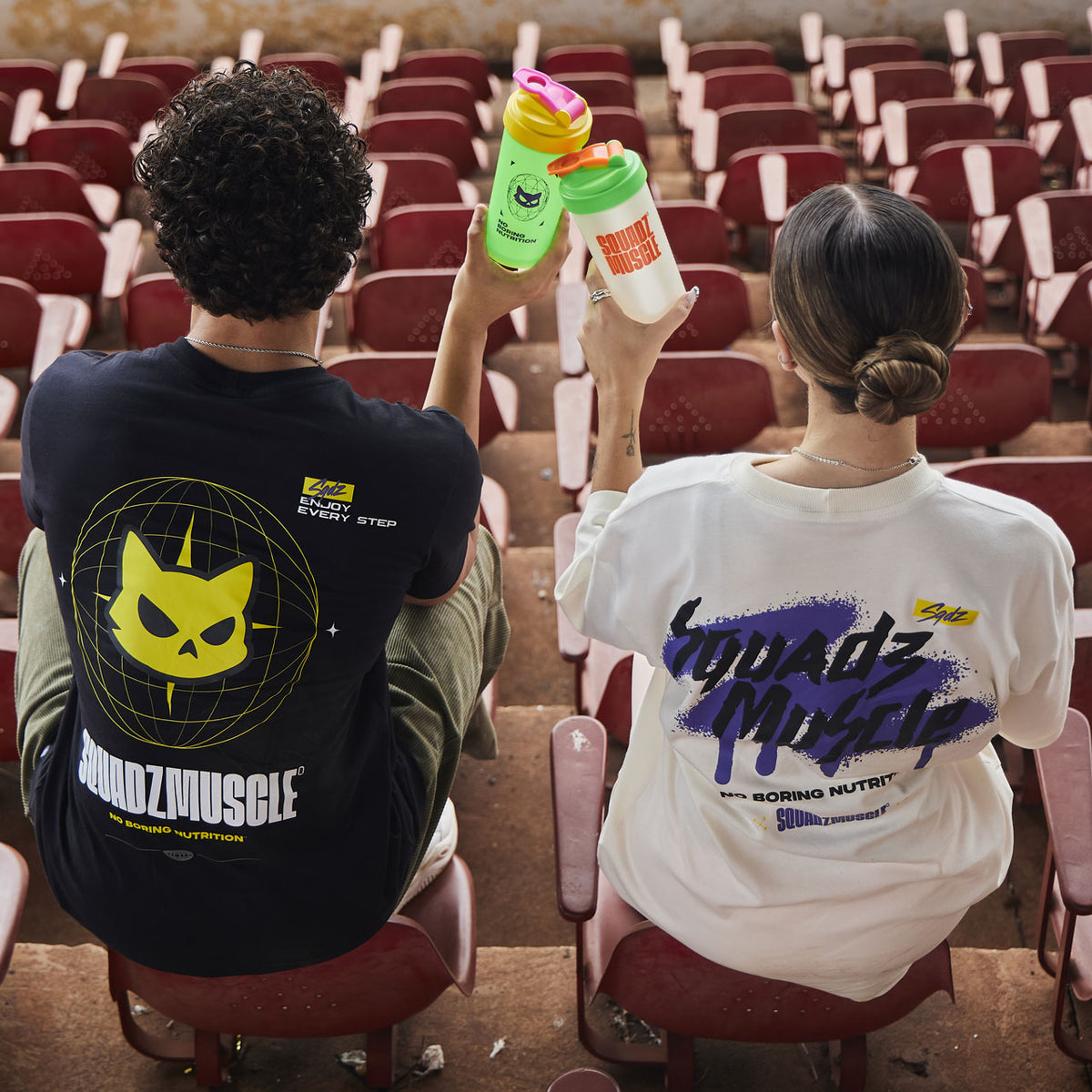 Duas pessoas de costas em arquibancada, com camisetas SQUADZ MUSCLE preta e branca