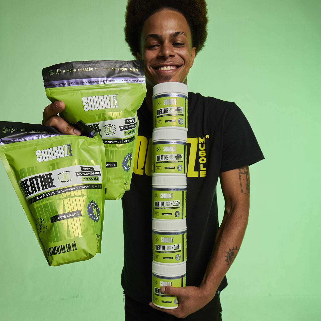 Homem sorrindo segurando o refil e uma torre de potes de Creatine SQUADZ MUSCLE