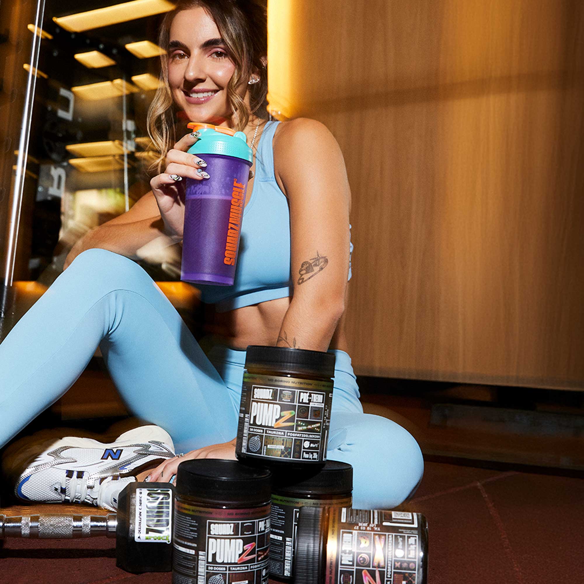 PUMP-Z Pré-Treino Tangerin Bomb 300g — Mulher na academia com os potes